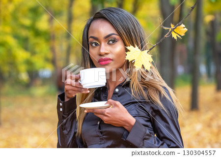 Woman enjoys tea in a serene autumn park surrounded by golden leaves 130304557