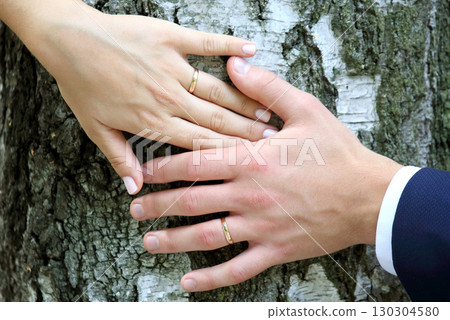 Couple placing their hands on a tree trunk to symbolize love and unity at an outdoor ceremony 130304580