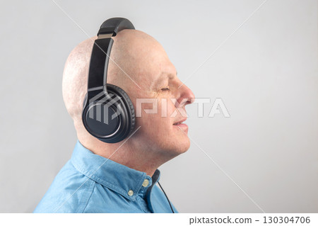 Middle-aged man enjoying music with headphones in a calm indoor setting Middle-aged man enjoying music with headphones in a calm indoor setting 130304706