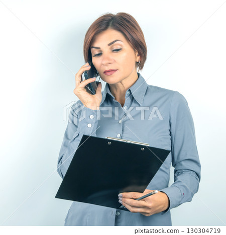 Professional woman engaged in a phone conversation while reviewing documents at work Professional woman engaged in a phone conversation while reviewing documents at work 130304719