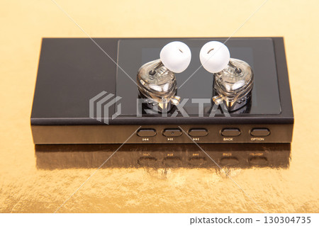 High-fidelity audio player with transparent earbuds on golden background 130304735