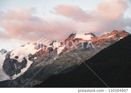 Early morning reveals stunning views of Piz Bernina, with its glacier-capped peaks illuminated by soft sunlight. The serene landscape showcases the beauty of the Swiss Alps. 130304807