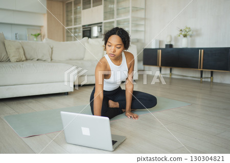 Yoga fitness workout training online. African woman practicing yoga with online lessons in laptop at home. Girl doing sports exercise on yoga mat. Woman have workout for weight loss. Sport fitness Yoga fitness workout training online. African woman practicing yoga with online lessons in laptop at home. Girl doing sports exercise on yoga mat. Woman have workout for weight loss. Sport fitness 130304821