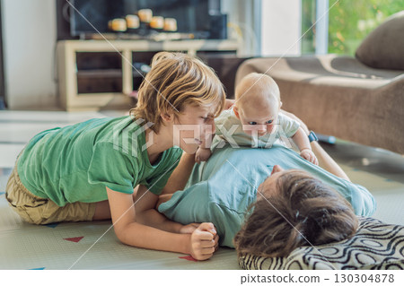 Father, son, and newborn baby lying on the floor in a cozy nursery, celebrating the arrival of their newest family member. Parenthood, bonding, and family love concept 130304878