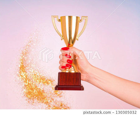 Woman's hand holding a trophy on a pink background with sparkling gold Woman's hand holding a trophy on a pink background with sparkling gold 130305032