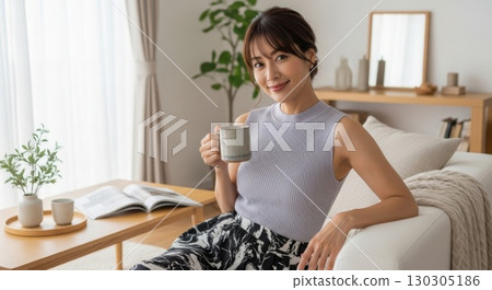 A beautiful woman in her 40s smiling with a mug in her hand on the sofa in the living room 130305186