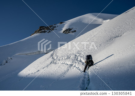 A climber makes their way up the steep, snowy ascent of Piz Palu in the Bernina Range during summer. Glaciers and alpine scenery surround the challenging route. A climber makes their way up the steep, snowy ascent of Piz Palu in the Bernina Range during summer. Glaciers and alpine scenery surround the challenging route. 130305841