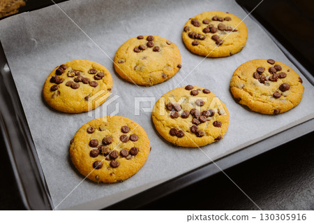 Freshly baked chocolate chip cookies in tray on parchment paper, closeup food photography 130305916