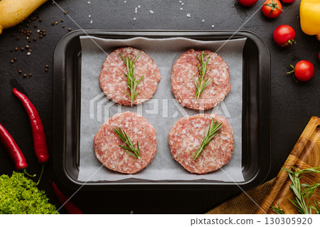 Raw pork burger patties with rosemary on parchment in a tray with vegetables and spices 130305920