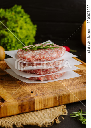 Stack of raw burger patties with rosemary on parchment paper, prepared for grilling 130305925