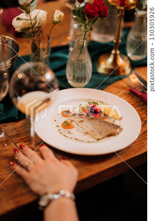 Elegant restaurant dinner with gourmet fish dish, wine glass, and festive table setting Elegant restaurant dinner with gourmet fish dish, wine glass, and festive table setting 130305926