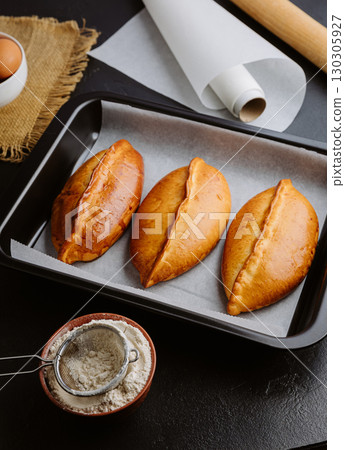 Freshly baked pies in baking tray, traditional homemade pastry with golden crust. Ukrainian piroshki Freshly baked pies in baking tray, traditional homemade pastry with golden crust. Ukrainian piroshki 130305927
