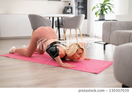 Middle aged woman in sportswear practicing cat pose on yoga mat at home, focusing on stretching her spine and back muscles Middle aged woman in sportswear practicing cat pose on yoga mat at home, focusing on stretching her spine and back muscles 130307039