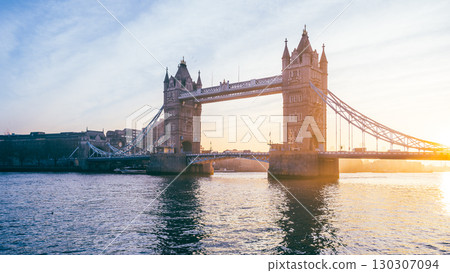 Tower Bridge stands majestically at sunrise, bathed in warm hues, with the River Thames reflecting the soft morning light in the heart of London, UK. 130307094