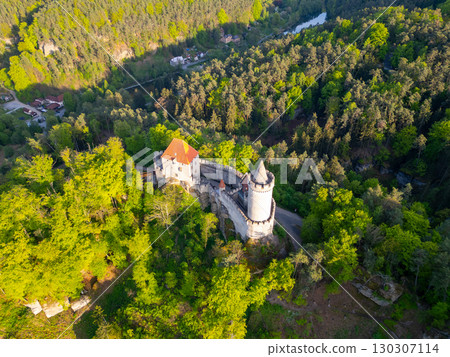 Golden sunlight bathes Kokorin Castle during a serene evening in Czechia. The aerial view showcases its medieval architecture surrounded by lush greenery and the winding landscape. 130307114