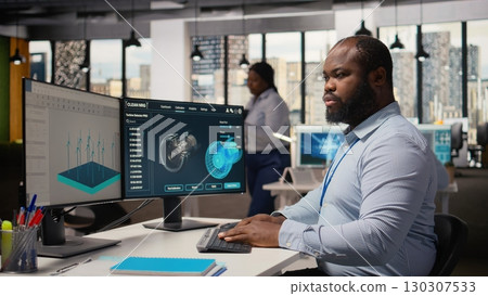 Renewable energy engineer in office upgrades windmill farm infrastructure with eco friendly turbines. RD department worker researching sustainable materials for wind power generation gear, camera A 130307533