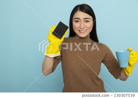 Pretty asian housekeeper standing calmly with coffee mug and cleaning sponge in hand, wearing yellow rubber gloves. Young female janitor enjoying peaceful break after long morning of household chores. Pretty asian housekeeper standing calmly with coffee mug and cleaning sponge in hand, wearing yellow rubber gloves. Young female janitor enjoying peaceful break after long morning of household chores. 130307539