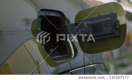 Close up of driver pushing electric car charging port flap to open it and recharge depleted battery. Person opens vehicle inlet port of EV automobile, preparing to resupply it with electricity Close up of driver pushing electric car charging port flap to open it and recharge depleted battery. Person opens vehicle inlet port of EV automobile, preparing to resupply it with electricity 130307577