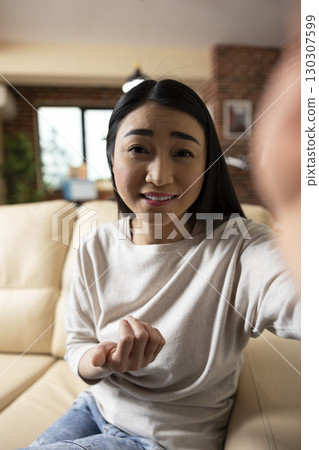 Pov of asian female freelancer with phone in hand, speaking to client on video call, providing updates on company project plans. Smiling businesswoman gestures to camera, engaging with online audience 130307599