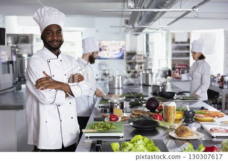 Portrait of young chef standing at the kitchen counter and preparing ingredients for a fine dining dish, skillfully cooking flavorful meal with precision and creativity. Delicious recipe. Portrait of young chef standing at the kitchen counter and preparing ingredients for a fine dining dish, skillfully cooking flavorful meal with precision and creativity. Delicious recipe. 130307617
