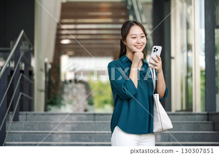 一位年輕女子在外出時查看她的智慧型手機 130307851