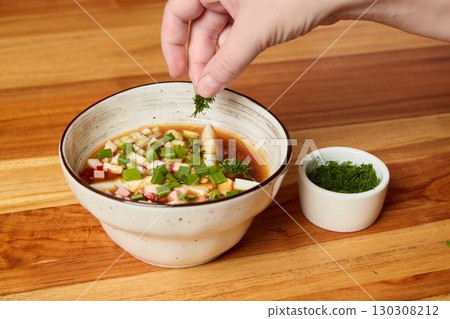 Enhancing a Bowl of Rich and Flavorful Soup with Freshly Cut Herbs for Added Aroma 130308212