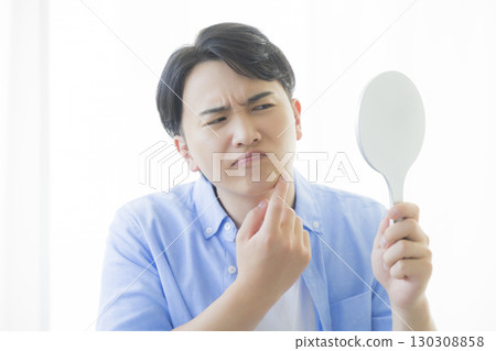 Man looking in a hand mirror 130308858