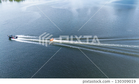 Aerial view of a boat pulling an Inflatable raft at a high speed in a recreational activity called tubing 130309019