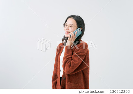 A woman in a sweater talking on a smartphone 130312293