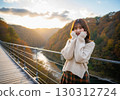 A woman in an autumn outfit posing cutely on a suspension bridge in a valley of autumn leaves 130312724