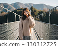 Autumn fashion portrait of a smiling woman wearing a beige knit on a suspension bridge 130312725