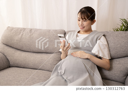 一名懷孕八個月的女子坐在沙發上,手裡拿著智慧型手機 一名懷孕八個月的女子坐在沙發上,手裡拿著智慧型手機 130312763