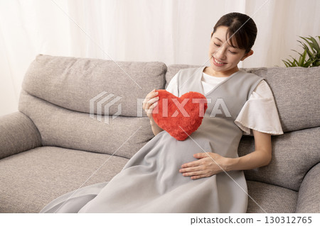 懷孕八個月的女人坐在沙發上，手裡拿著一顆紅心 130312765