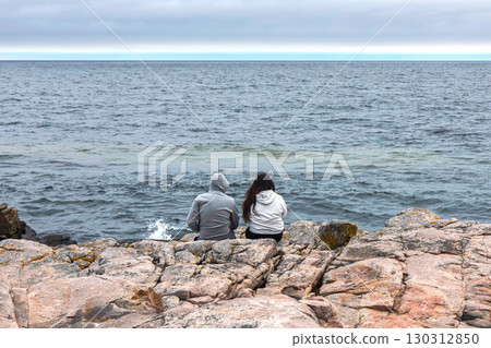 Couple in love, a man and a woman are sitting on a rocky seashore 130312850