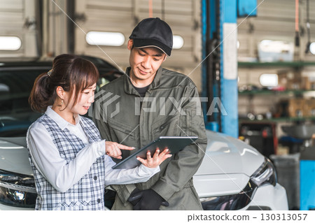 Male and female employees looking at a tablet in the pit of a maintenance workshop (automobile maintenance workshop, private vehicle inspection center, staff) 130313057