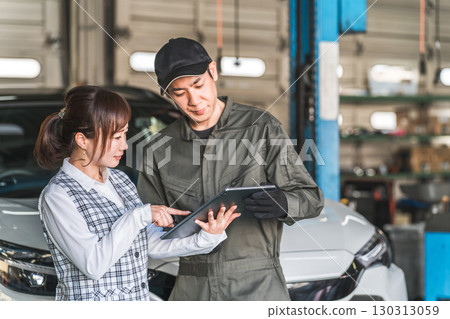 Male and female employees looking at a tablet in the pit of a maintenance workshop (automobile maintenance workshop, private vehicle inspection center, staff) 130313059