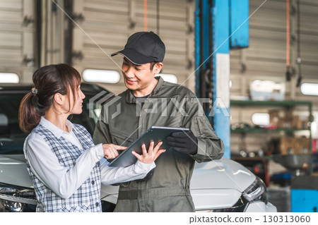 Male and female employees looking at a tablet in the pit of a maintenance workshop (automobile maintenance workshop, private vehicle inspection center, staff) 130313060
