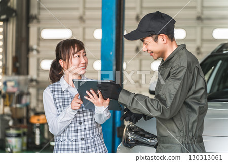 Male and female employees looking at a tablet in the pit of a maintenance workshop (automobile maintenance workshop, private vehicle inspection center, staff) 130313061