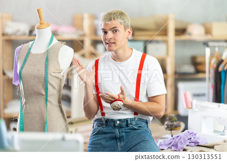 Young male dressmaker half-sitting at his workplace in sewing workshop Young male dressmaker half-sitting at his workplace in sewing workshop 130313551