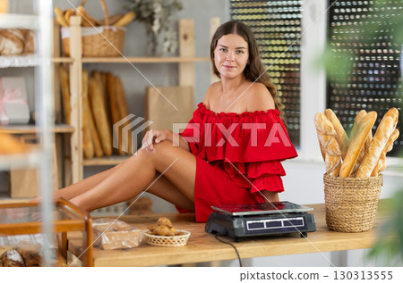 Woman in red dress sitting on counter in bakery 130313555