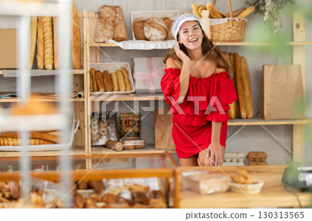 Smiling happy girl in red dress behind bakery counter Smiling happy girl in red dress behind bakery counter 130313565