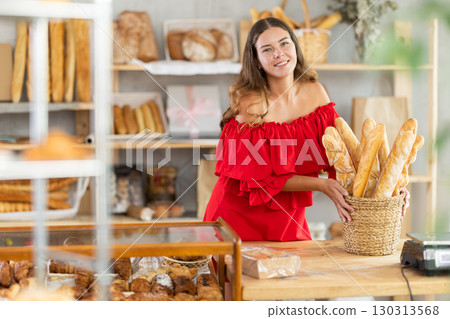 Girl in red dress with bare shoulders stands at table in sales area of bakery 130313568