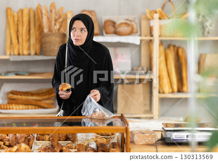 European Muslim young woman in hijab visitor puts croissant in plastic disposable bag European Muslim young woman in hijab visitor puts croissant in plastic disposable bag 130313569