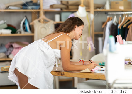 Dressmaker draws a model of clothes on paper in a workshop 130313571