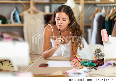 Seamstress calculating garment measurements with smartphone and notes Seamstress calculating garment measurements with smartphone and notes 130313582