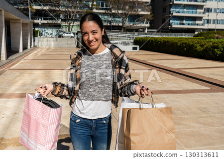Young woman smiling and holding shopping bags in a city setting 130313611