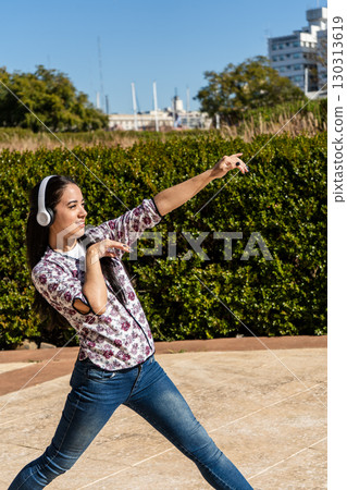 Young latin woman dancing with headphones in a park, enjoying music and freedom 130313619