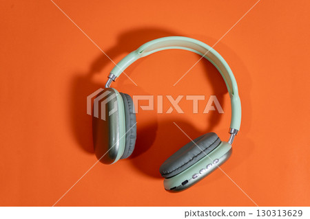 Modern wireless headphones lying on vibrant orange background Modern wireless headphones lying on vibrant orange background 130313629