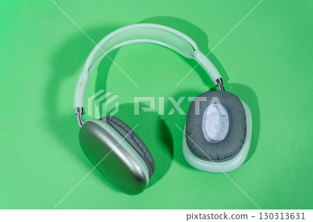 Modern wireless headphones lying on vibrant green background 130313631