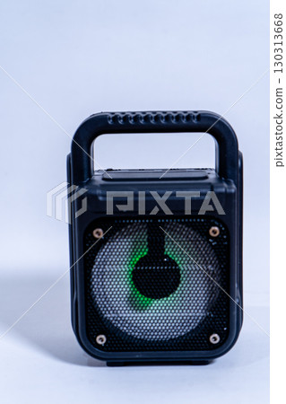 Black portable speaker with handle and green light showing on white background 130313668